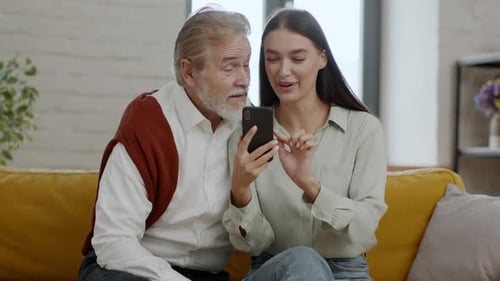 Woman and Senior Man Laughing at Smartphone Indoors