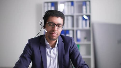 Customer Support African American Man in Glasses Works in a Call Center and Talks on Headset with