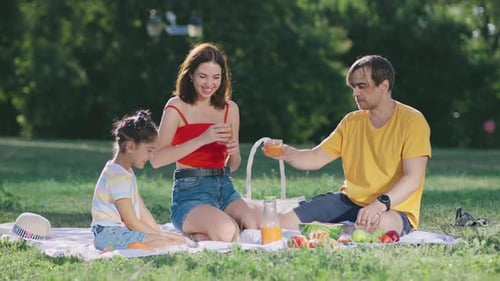 Family Enjoys a Sunny Picnic in the Park Savoring Fresh Fruit and Refreshing Drinks with Laughter
