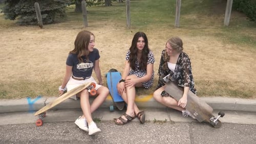 Three teenage girls sit with skateboards and talk