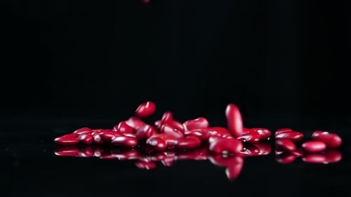Red Kidney Beans Falling on Black Reflective Surface