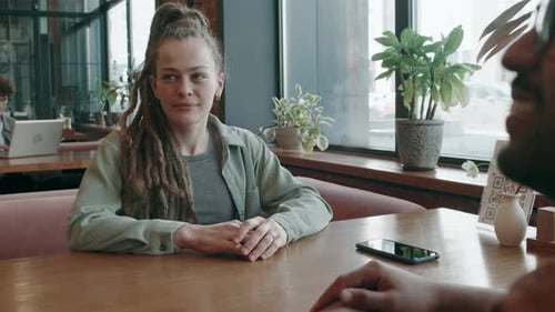 Two Friends Sitting at Table in Cafe, Smiling as Waiter Handing them Paper Menu