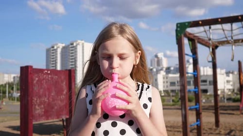 Girl Blowing Up a Pink Balloon on Playground
