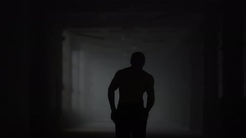 Silhouette of fitness man running cardio workout in dark loft building corridor