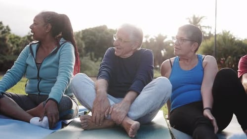 Happy senior people after yoga sport class having fun sitting in public park. Elderly fitness