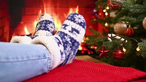 Legs in Jeans and Warm Woolen Socks with a Scandinavian Ornament Against the Background of a Red