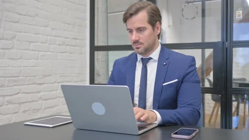 Focused Man Typing on Laptop in Office