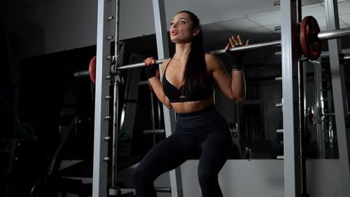 The Silhouette of a Woman in Black Workout Clothes Squatting in a Gym