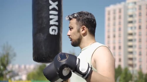 Man Training Boxing Punches with Punching Bag Outdoors