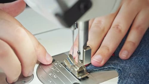 A Closeup Shot of a Seamstress's Hands Working with Sewing Machines on a Piece of Denim Fabric Which