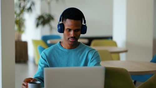Man with Headphones Drinks Coffee While Working