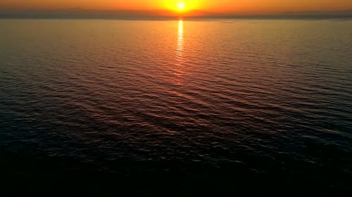 Tilt up drone shot of a stunning sunset in Greece over the ocean, with birds flyng accross and a dis