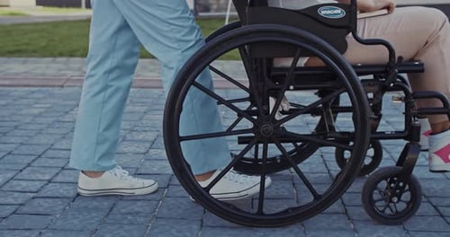 Attendant Pushes Wheelchair Patient on Paved Path