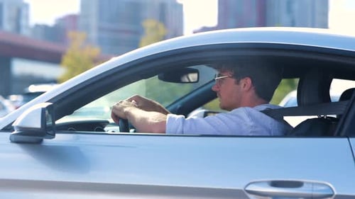 Happy Young Man in Glasses Driving His Car with Open Window Looking on the Road Side View Transport