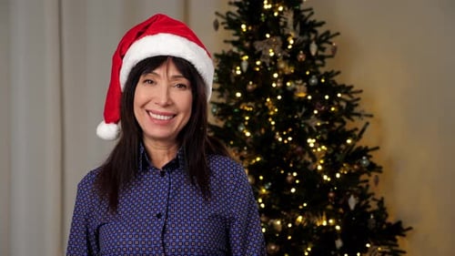 Woman in Santa Hat Smiles by Christmas Tree