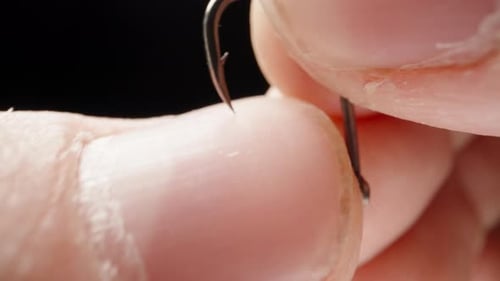 Checking the sharpness of a fishing hook on a finger, close-up.