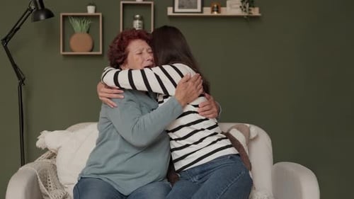 Woman Hugs Grandmother on White Couch Indoors