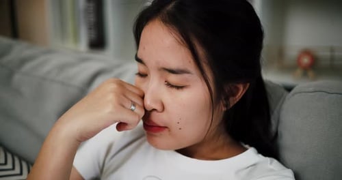 Worried Woman with Headache Sits on Couch