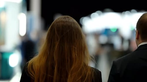 Two Attendees Seen From Behind Navigating a Modern Exhibition Hall Moving Between Booths Under Soft