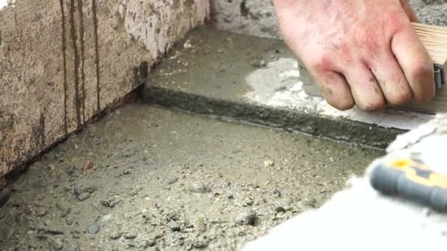 Construction Worker Hands Smooth Wet Cement in Wooden Frame at a Construction Site During Daytime to