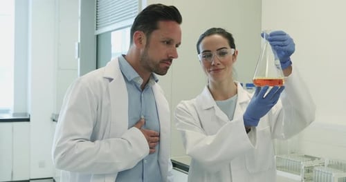 Female scientist analyzing liquid in conical flask with a male colleague
