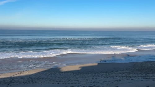 Waves creeping steadily across open beach on a sunny day