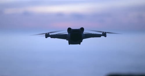 Silhouette einer modernen Quadcopter-Drohne vor dem Hintergrund der Morgendämmerung auf dem Meer im Urlaub
