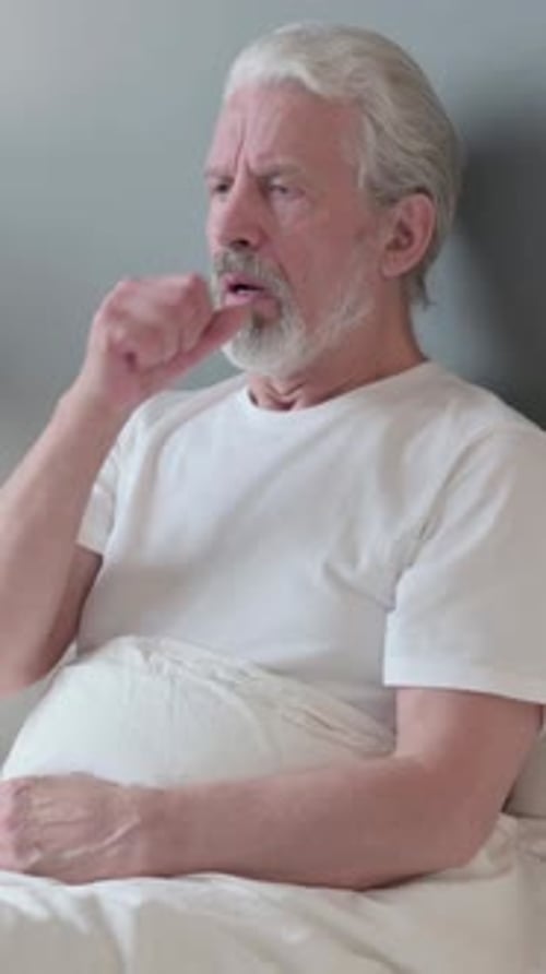 Senior Man in Bed Coughing, Feeling Unwell Indoors