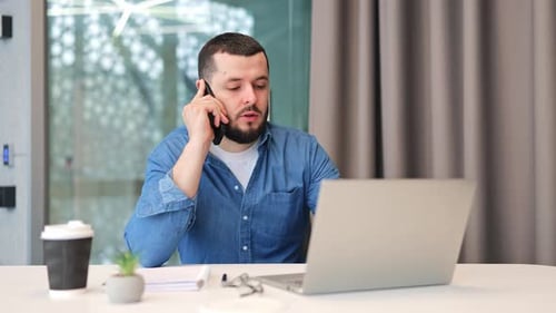 Man Talking on Phone While Using Laptop at Desk