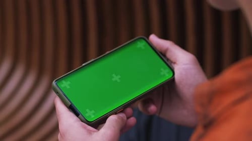 Hand Man Holding a Smartphone Touching Phone with Horizontal Green Screen Phone on Background Street