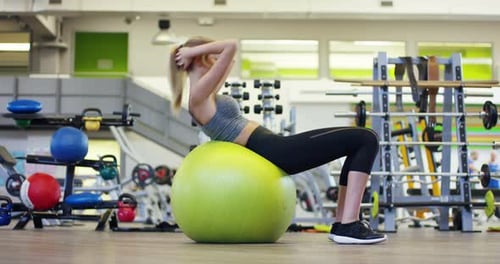 Young beautiful girl in the gym, swings the press with the ball for fitness, improving the muscles