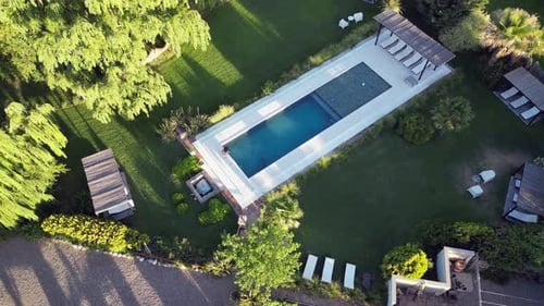 Aerial pulls in as woman tests swimming pool water in landscaped yard
