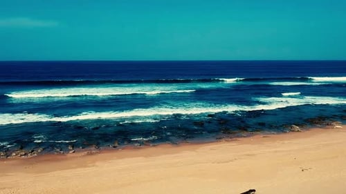 Aerial footage filmed with a drone overlooking the beach and sea of crashing waves with a deep blue