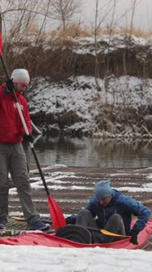 Vídeo vertical: Dos jóvenes de complexión atlética sentados en una escena invernal en kayak rojo