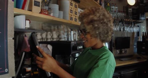 Feliz camarera afroamericana usando una caja registradora mientras trabajaba en un bar