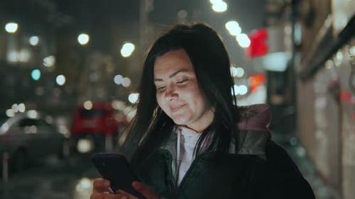 Woman Uses Smartphone on City Street at Night