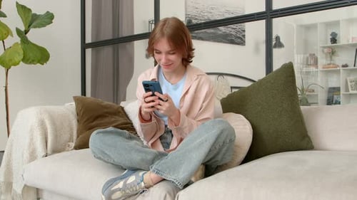 Adorable Teenage Girl Online Messaging on Mobile Phone Phone on Sofa at Home