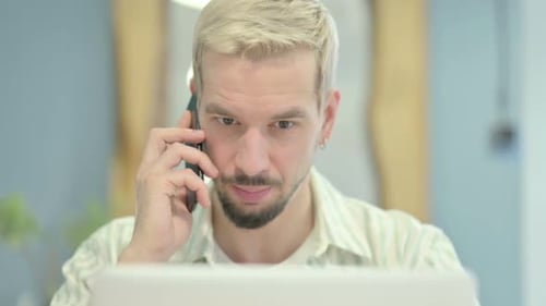Close Up of Young Man Talking on Phone while using Laptop