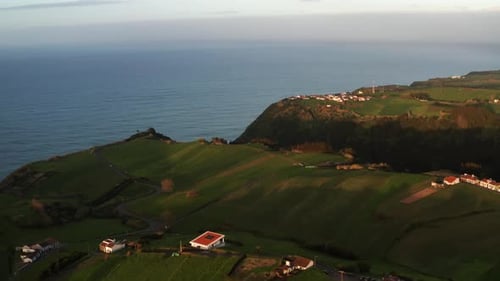 Imagens de drone da paisagem verdejante de uma ilha vulcânica ao pôr do sol com casas perto de um penhasco oceânico no