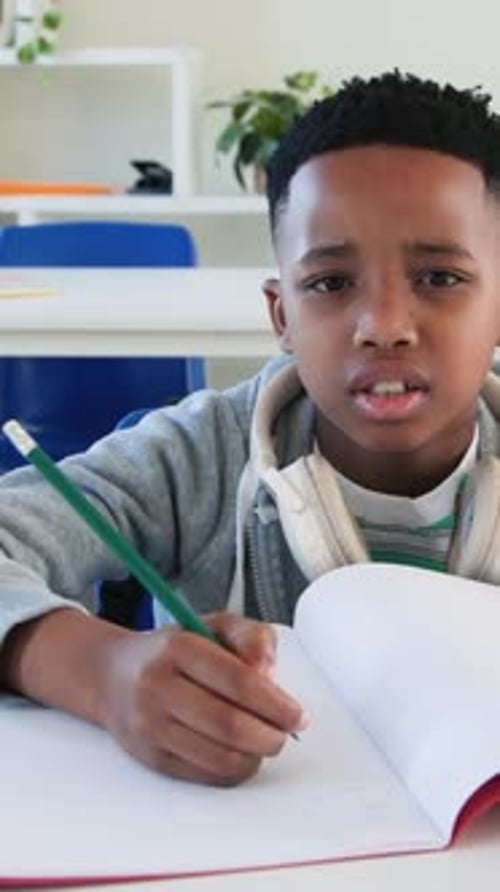 Vertical video: Writing hoodie kid solving math at desk, counting fingers with green pencil