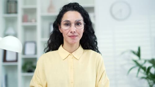 Close up portrait of young smiling woman in glasses at home. Headshot of a friendly female freelance
