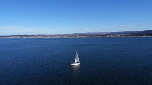 Sailboat glides across monterey bay California waters under sunny skies drone view