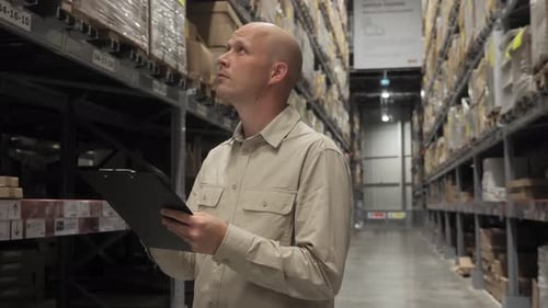 A Male Employee Checks the Stocks in the Retail Warehouse of Shelves with Goods