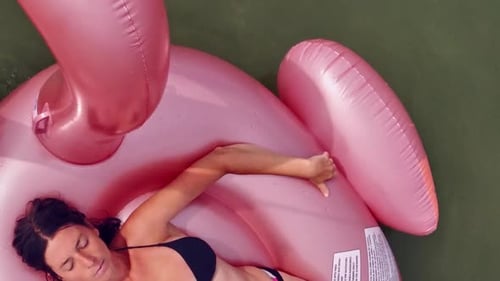 High angle view of woman lying and relaxing on pink inflatable flamingo floating and circling alone