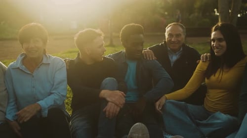 Happy multi generational people having fun sitting on the grass in a public park