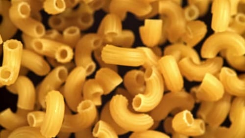 Uncooked elbow macaroni on black background zooming in