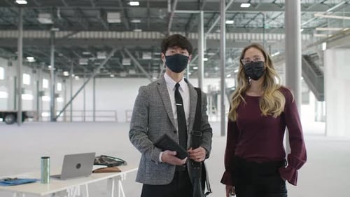 Confident real estate investors wearing face masks panning in warehouse