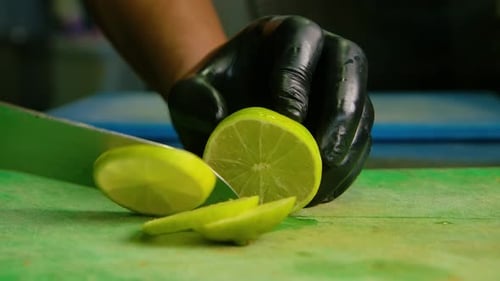Der Koch in schwarzen Latexhandschuhen schneidet Zitrone oder Limette sauber in mittelgroße runde Scheiben