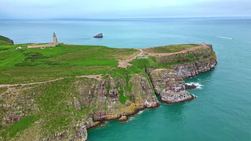 Panorama-Drohnenbewegung rund um die felsige Halbinsel Cap Fréhel und ihren Leuchtturm, umgeben von Beau