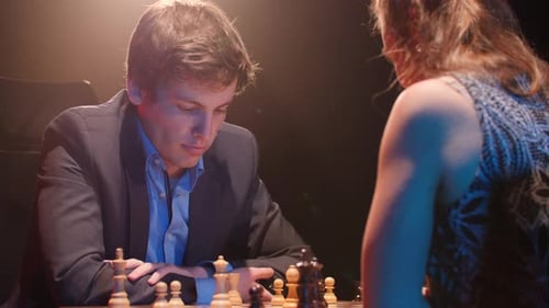 Un homme en costume fait un mauvais pas dans un tournoi d'échecs contre une jeune femme sous les projecteurs